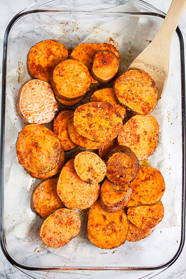 Sweet potato rounds tossed with olive oil and spices in glass cake pan.