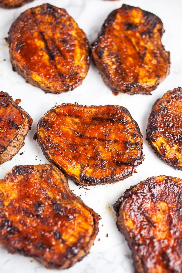 Grilled sweet potato rounds with BBQ sauce on white surface.