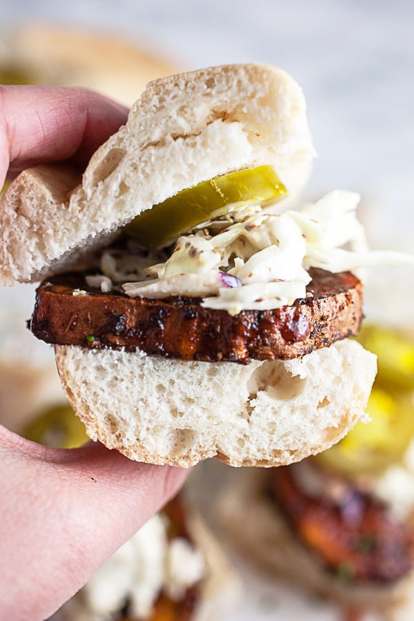 Hand holding a BBQ sweet potato sandwich with coleslaw and pickled jalapenos.