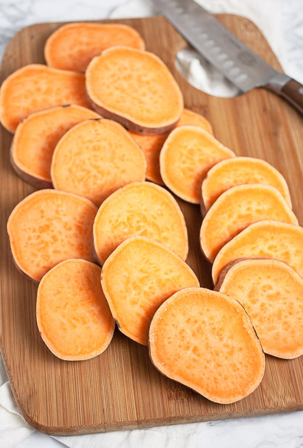 Sliced sweet potato rounds on wooden cutting board with knife.