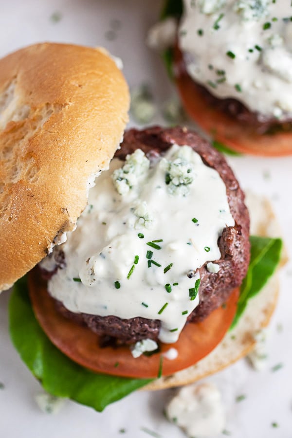 Grilled beef burger on bun with lettuce, tomato, and creamy blue cheese sauce.