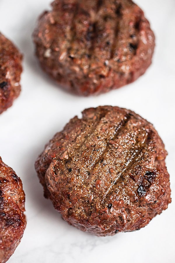 Grilled beef burgers on white surface.