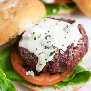 Grilled burgers on buns with lettuce, tomato, and blue cheese sauce.