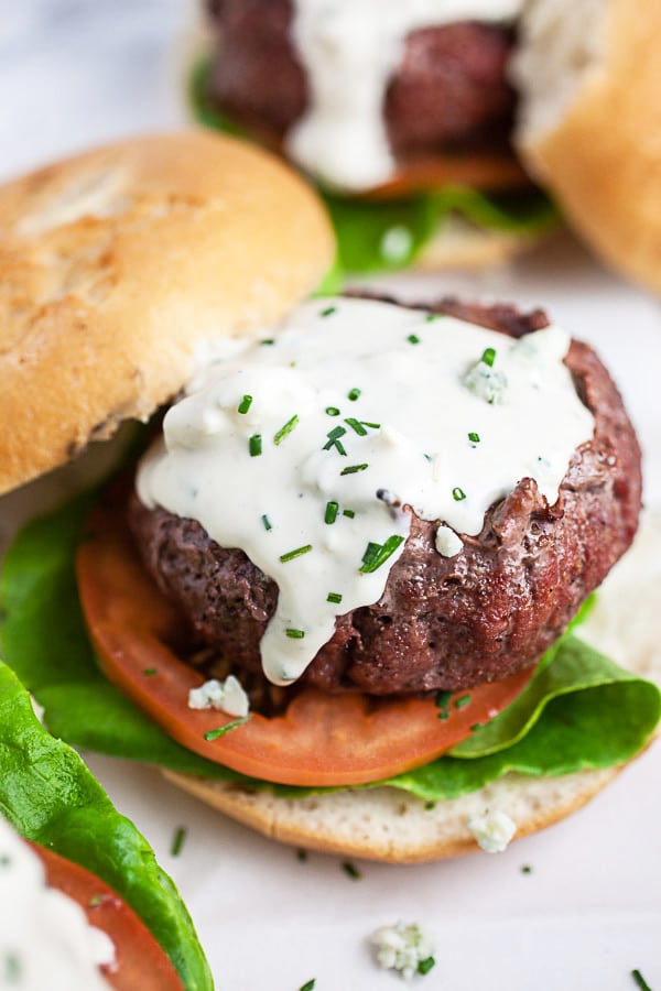 Grilled burgers on buns with lettuce, tomato, and blue cheese sauce.