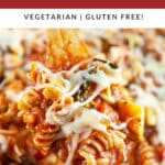 Scoop of cheesy veggie pasta lifted from skillet on wooden spoon.