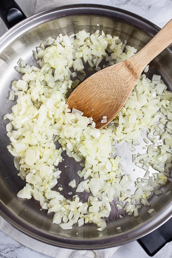 Sautéed garlic and onions in skillet with wooden spatula.