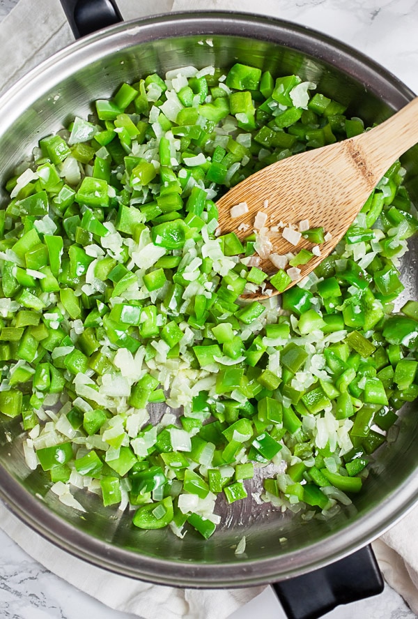 Garlic, onions, and green bell peppers sautéed in skillet with wooden spatula.