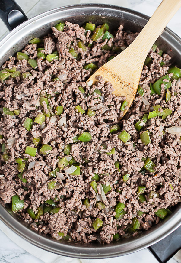 Ground beef and peppers sautéed in skillet with wooden spatula.