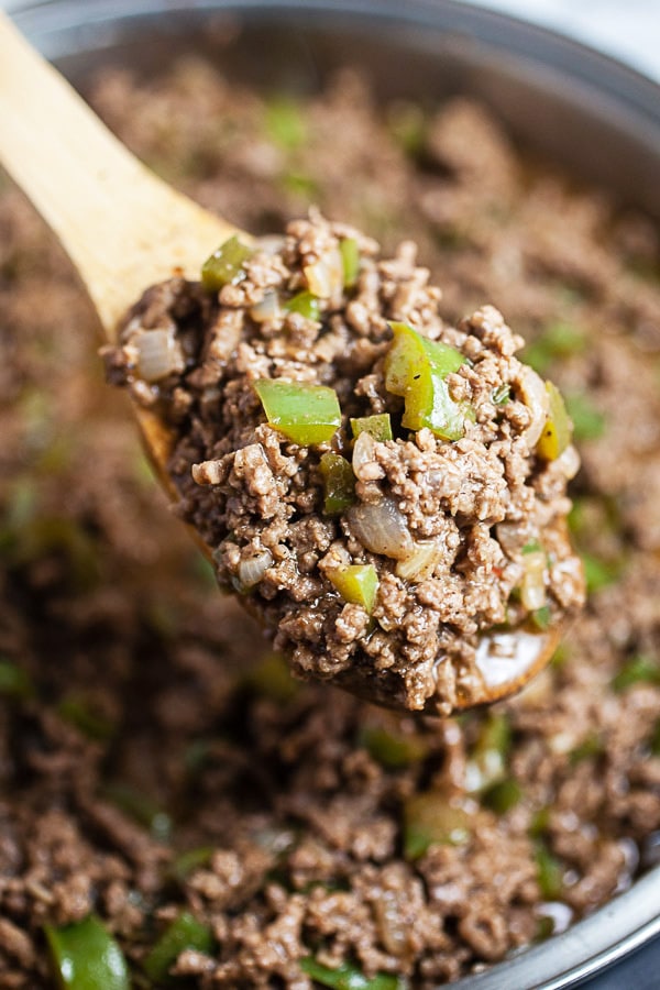 Spoonful of cooked ground beef sloppy joes lifted from skillet.