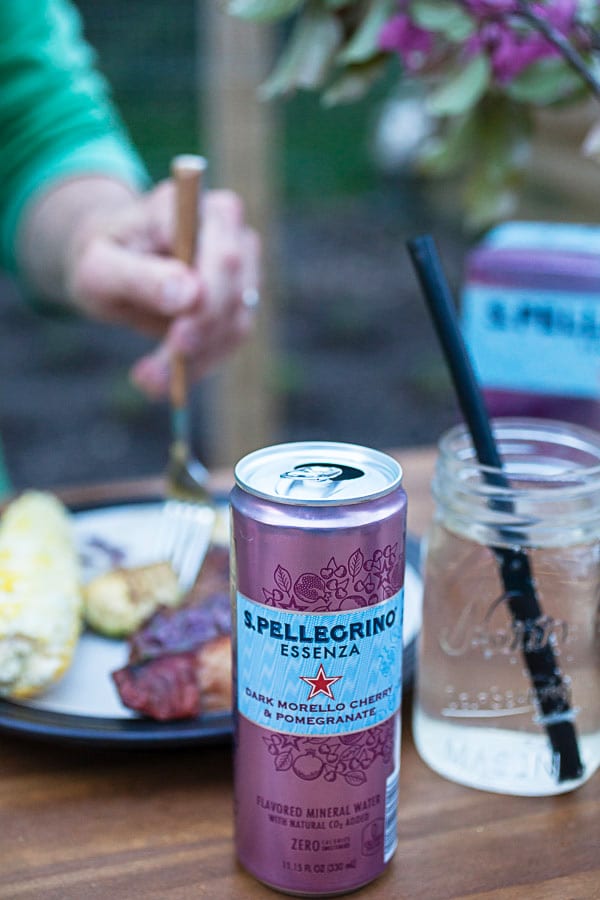 Can of sparkling water in front of man eating steak off a plate on an outdoor table.