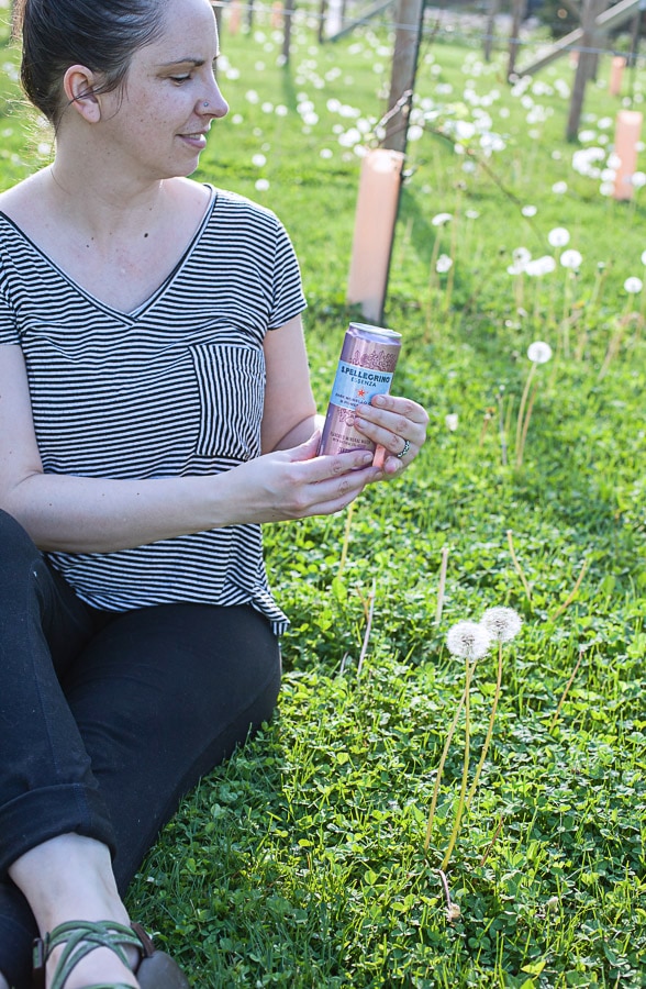 Woman sitting on grass holding can of sparkling water.