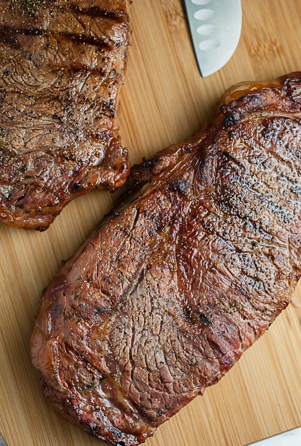 Grilled ribeye steaks resting on wooden cutting board.