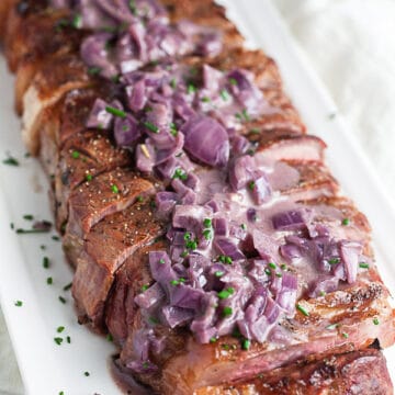 Sliced grilled ribeye steak topped with shallot sauce on white serving platter.