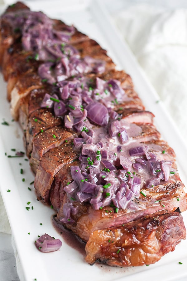 Sliced grilled ribeye steak topped with shallot sauce on white serving platter.