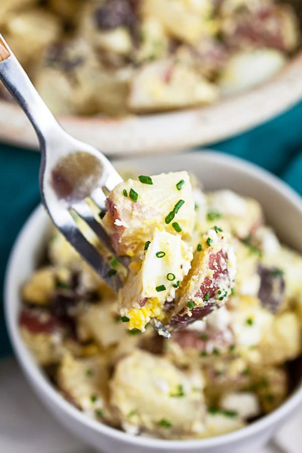 Forkful of potato salad lifted from small white bowl.