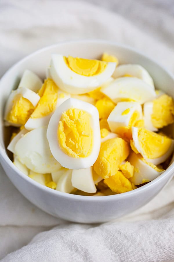 Hard boiled eggs cut into pieces in small white bowl.