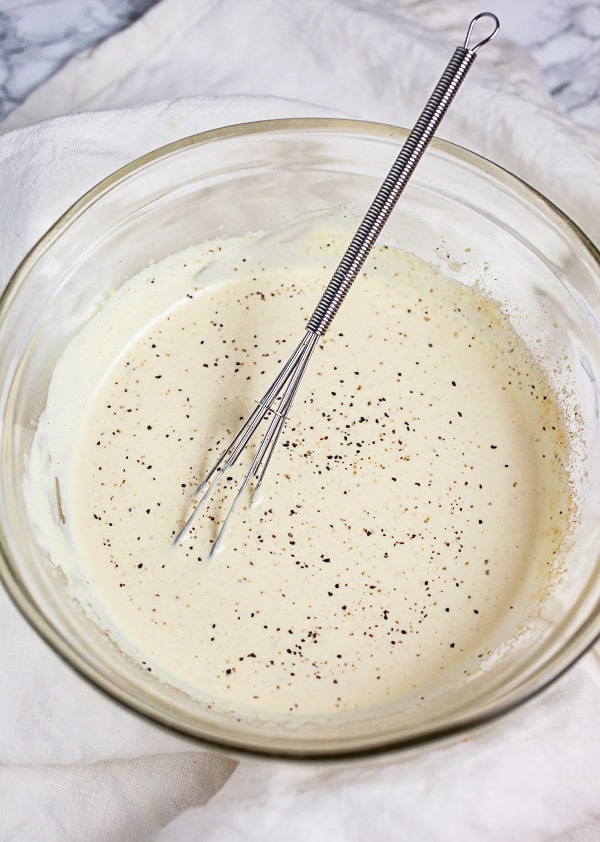 Creamy lemon dressing in small glass bowl with whisk.