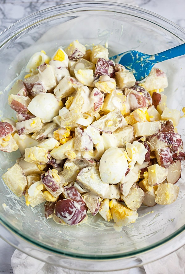 Cooked potatoes and eggs tossed with dressing in large glass mixing bowl.