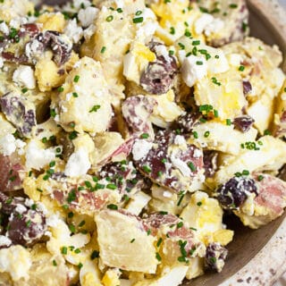 Mediterranean potato salad with eggs, Kalamata olives, and feta in ceramic bowl.