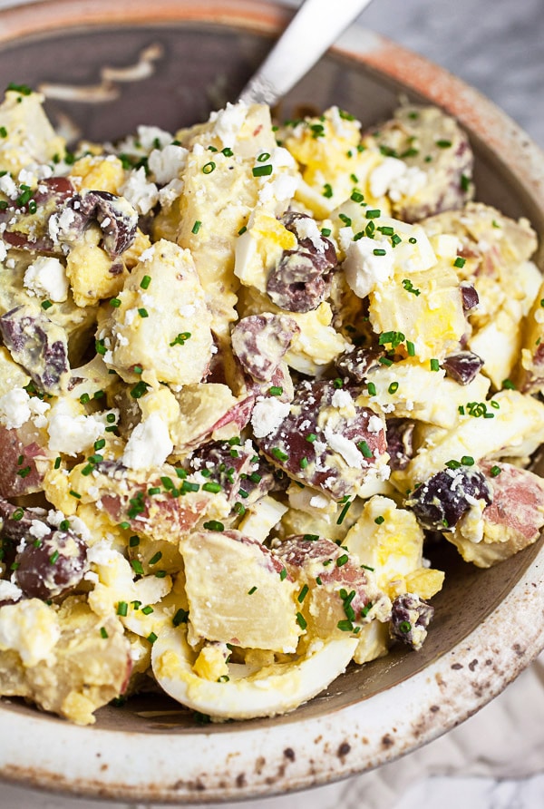 Mediterranean potato salad with eggs, Kalamata olives, and feta in ceramic bowl.