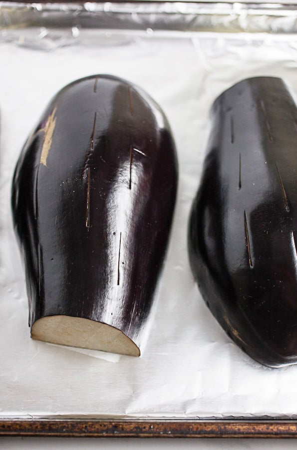 Halved eggplant on foil lined baking sheet with slits cut in skin.