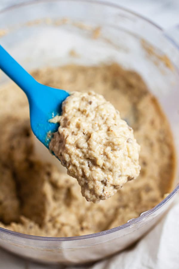 Scoop of baba ghanoush lifted from food processor with blue spatula.