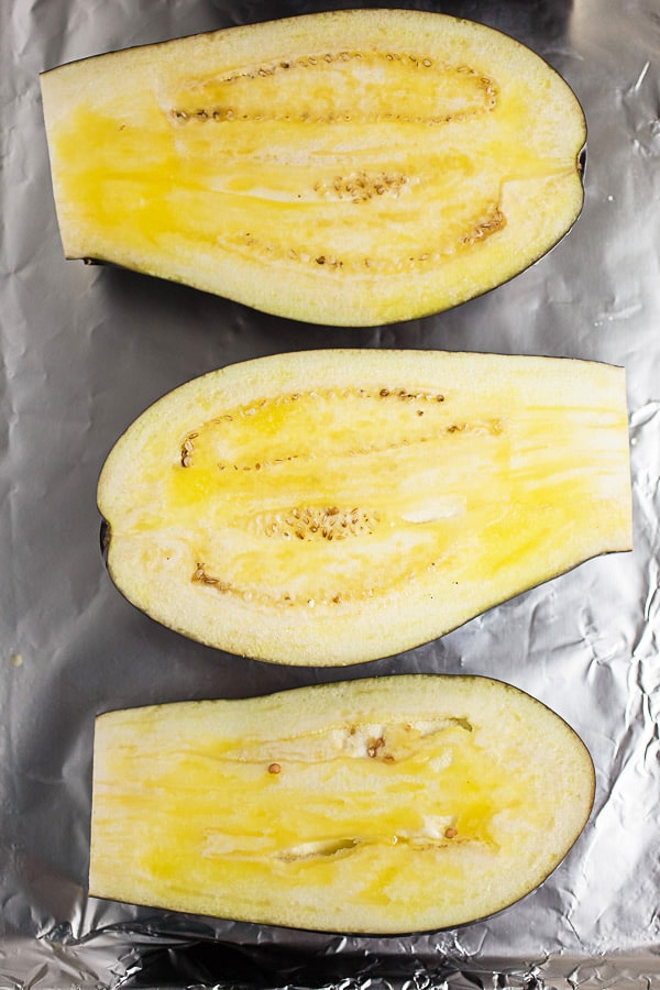 Eggplant cut in half and topped with olive oil on foil lined baking sheet.