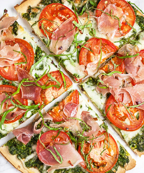 Arugula pesto pizza with tomatoes and prosciutto cut into slices.