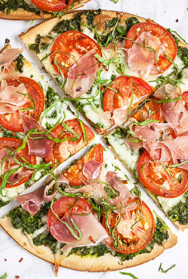 Arugula pesto pizza with tomatoes and prosciutto cut into slices.