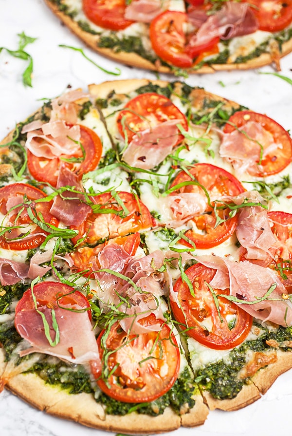 Baked arugula pesto pizzas cut into slices on white surface.