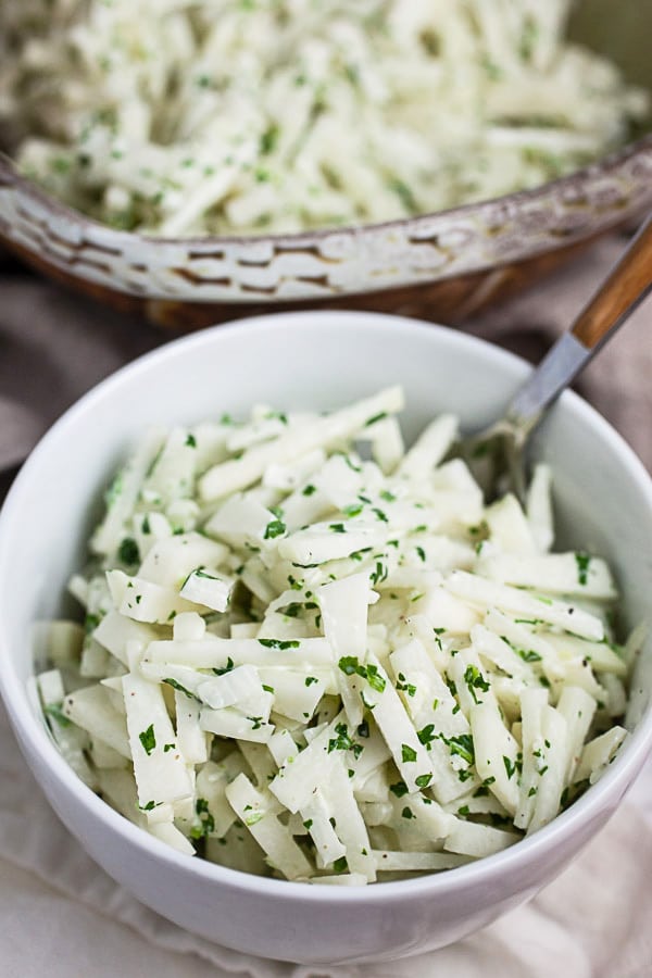 Kohlrabi slaw in small white bowl next to larger ceramic bowl.