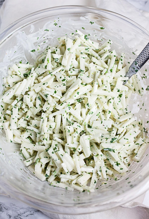 Kohlrabi coleslaw with cilantro lime dressing in large glass mixing bowl.