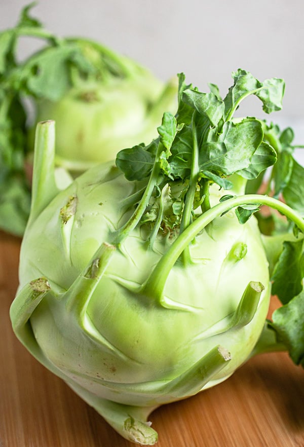 Two whole kohlrabi on wooden cutting board.