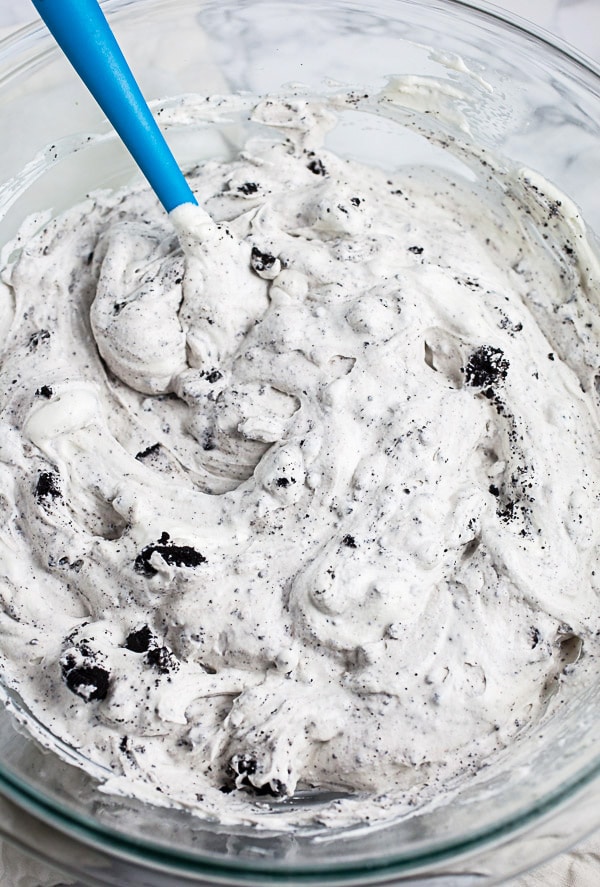 Crushed chocolate sandwich cookies mixed together with ice cream in large glass bowl.