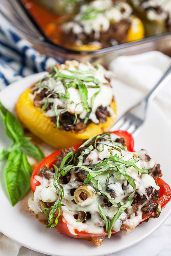 Pizza stuffed peppers with fresh basil on small white plate with fork.