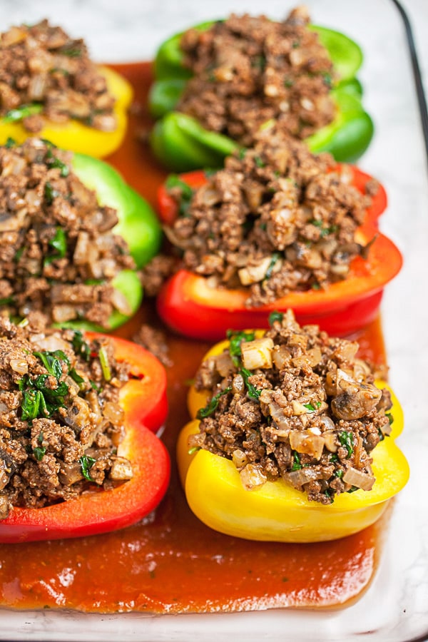 Uncooked bell peppers stuffed with ground beef in glass baking dish.