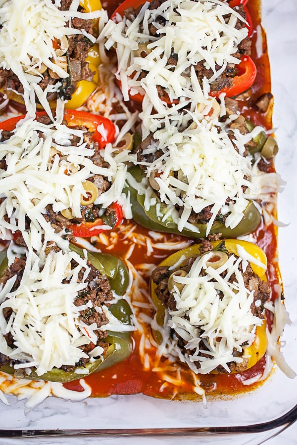 Baked stuffed peppers topped with shredded mozzarella cheese in glass baking dish.