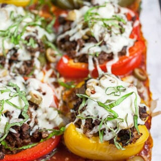 Baked bell peppers in pizza sauce topped with fresh basil in glass baking dish.