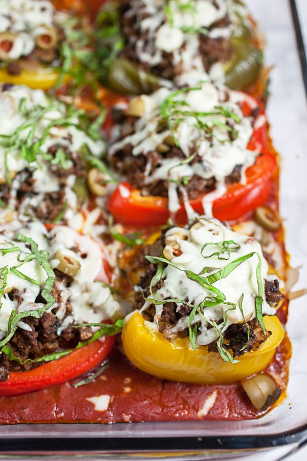 Baked bell peppers in pizza sauce topped with fresh basil in glass baking dish.