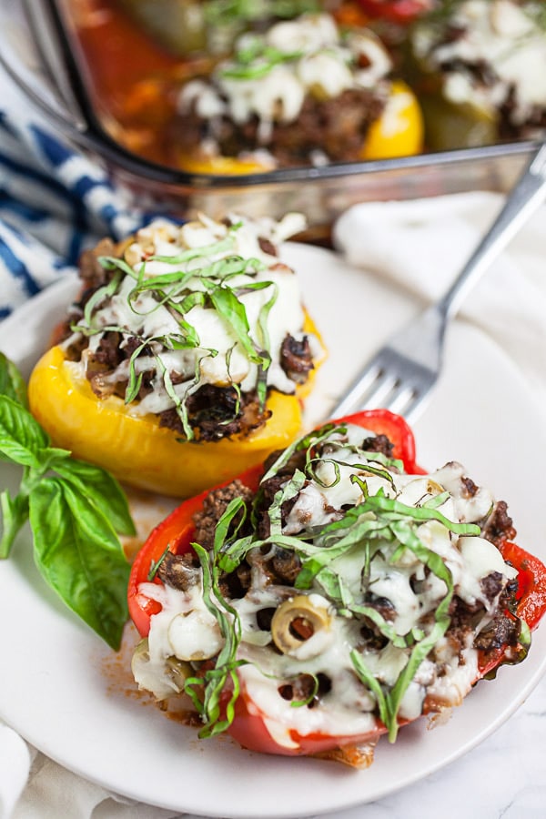 Ground beef stuffed red and yellow bell peppers with fresh basil on small white plate.