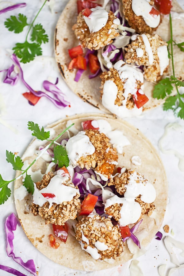 Crispy shrimp tacos on corn tortillas with sauce, cilantro, and red cabbage.