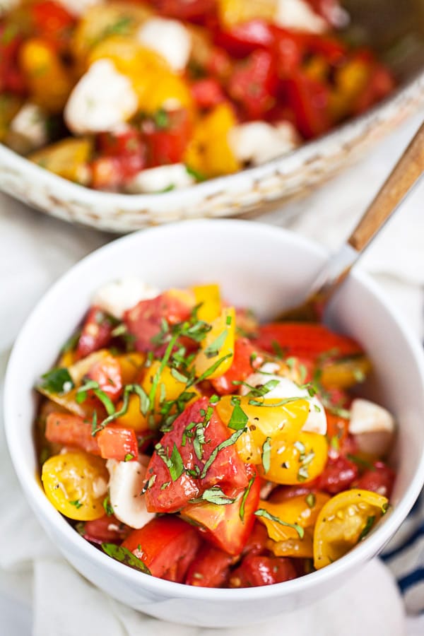 Tomato basil salad in small white bowl next to larger ceramic bowl.