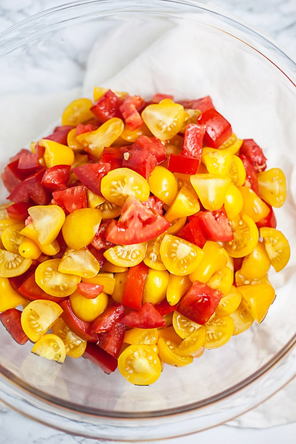 Chopped Roma and yellow pear tomatoes in large glass bowl.