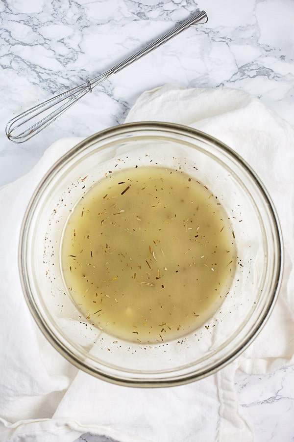 Olive oil, vinegar, garlic, and Italian herb dressing mixed in small glass bowl.