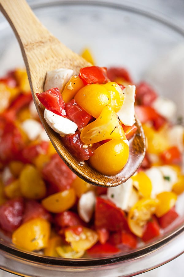 Scoop of tomato mozzarella salad lifted from glass bowl with wooden spoon.