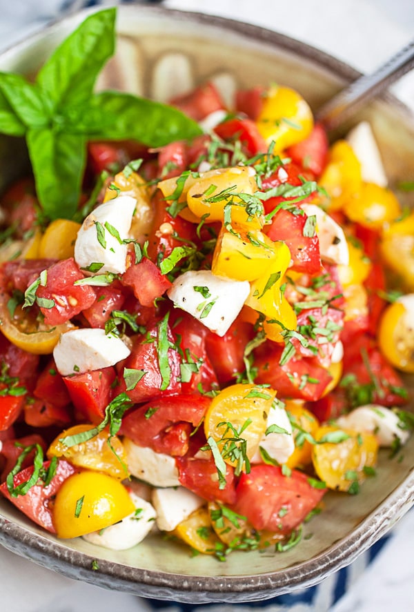 Marinated tomato salad with mozzarella and fresh basil in ceramic bowl.