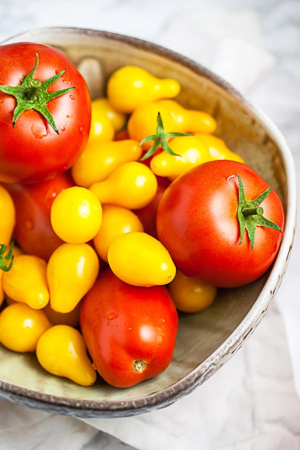 Fresh Roma and yellow pear tomatoes in ceramic bowl.