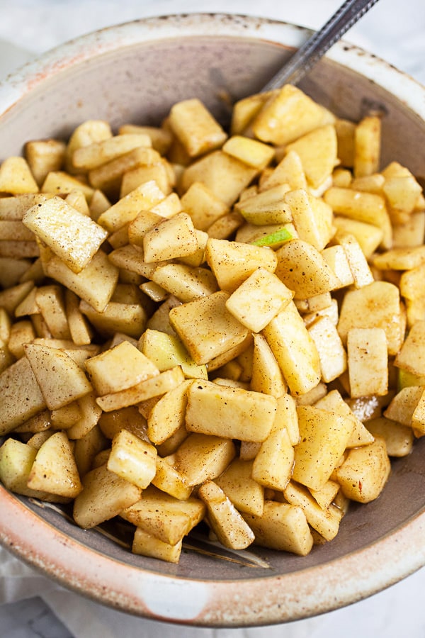 Unbaked apple pie filling with spices in ceramic bowl.