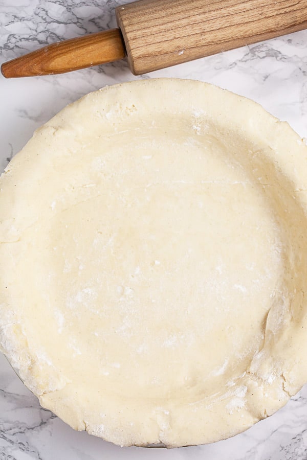 Unbaked gluten free pie crust in pie plate next to wooden rolling pin.