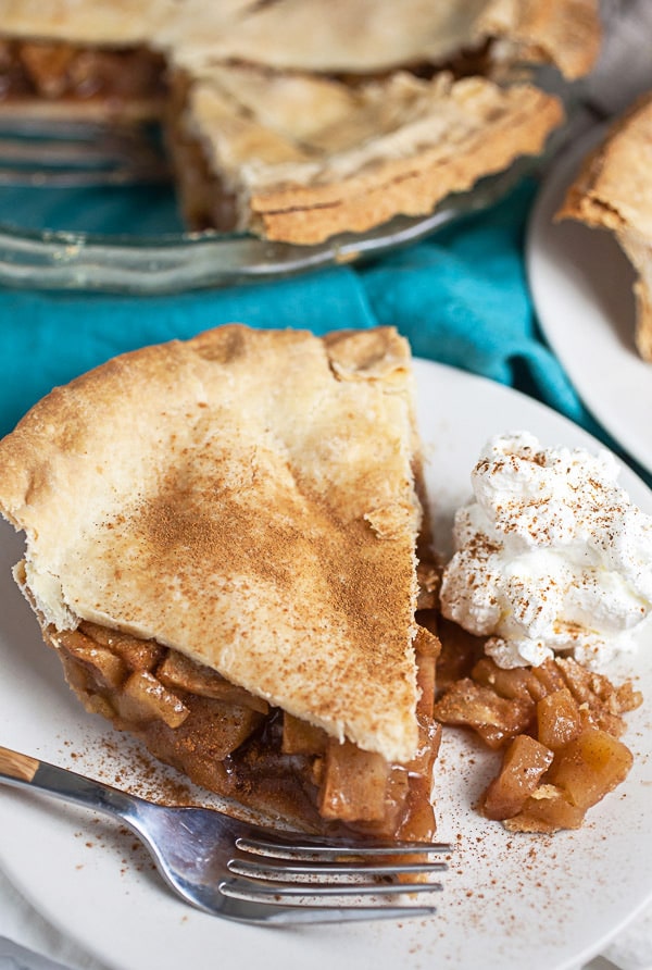 Apple pie with whipped cream on small white plate with fork.